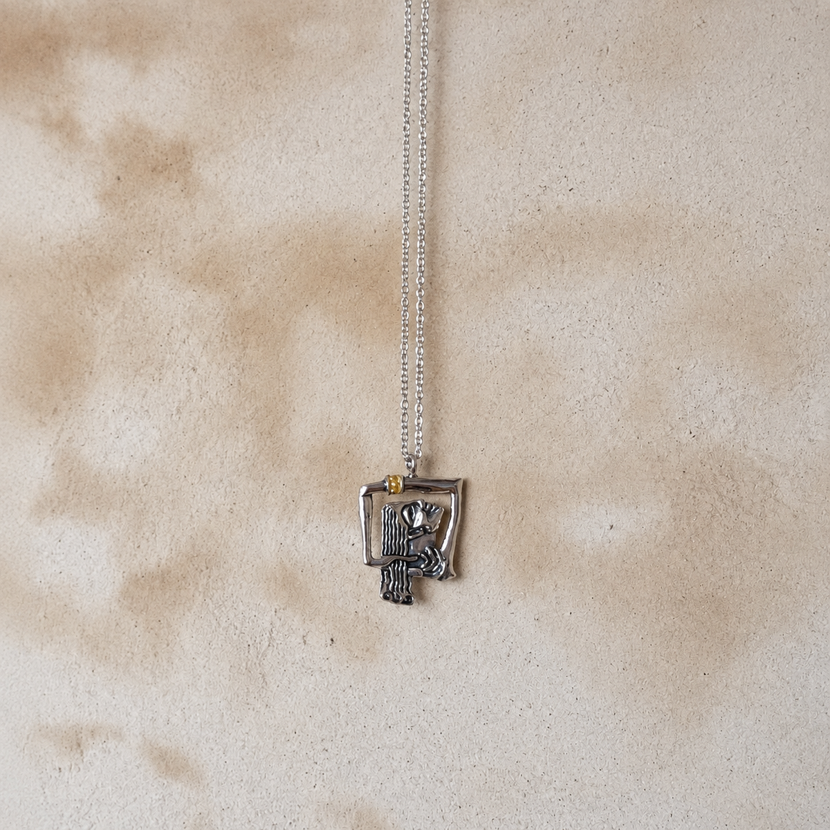Silver-tone abstract woman pendant necklace with a small gold-tone accent on a neutral background Bali inspired stone 