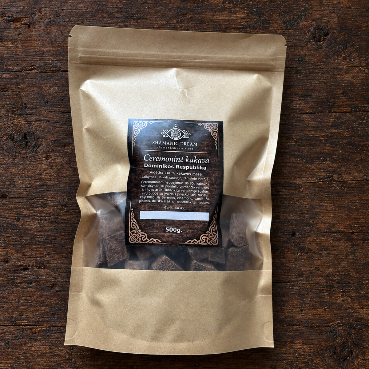 500 g pouch of Shamanic Dream ceremonial cacao from the Dominican Republic, shown on a dark aged wood surface.
