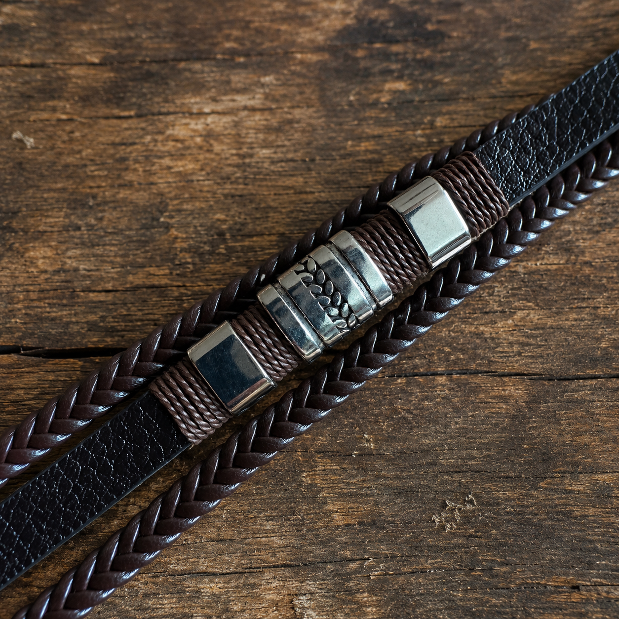 Close-up of a handcrafted dark brown leather bracelet with braided leather and metal accents on a wooden surface