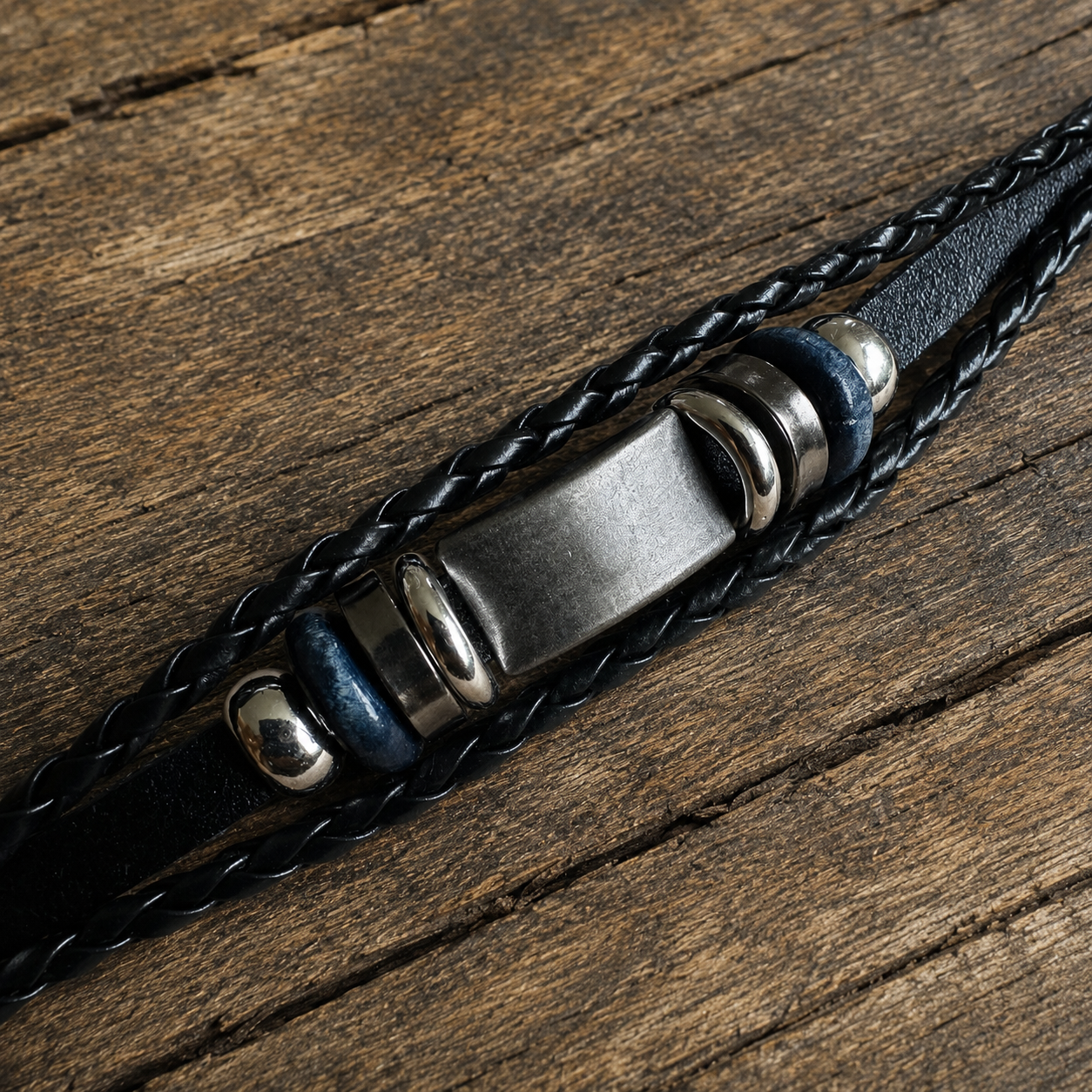 Handcrafted navy black leather bracelet with braided leather and metallic accents on a wooden surface.