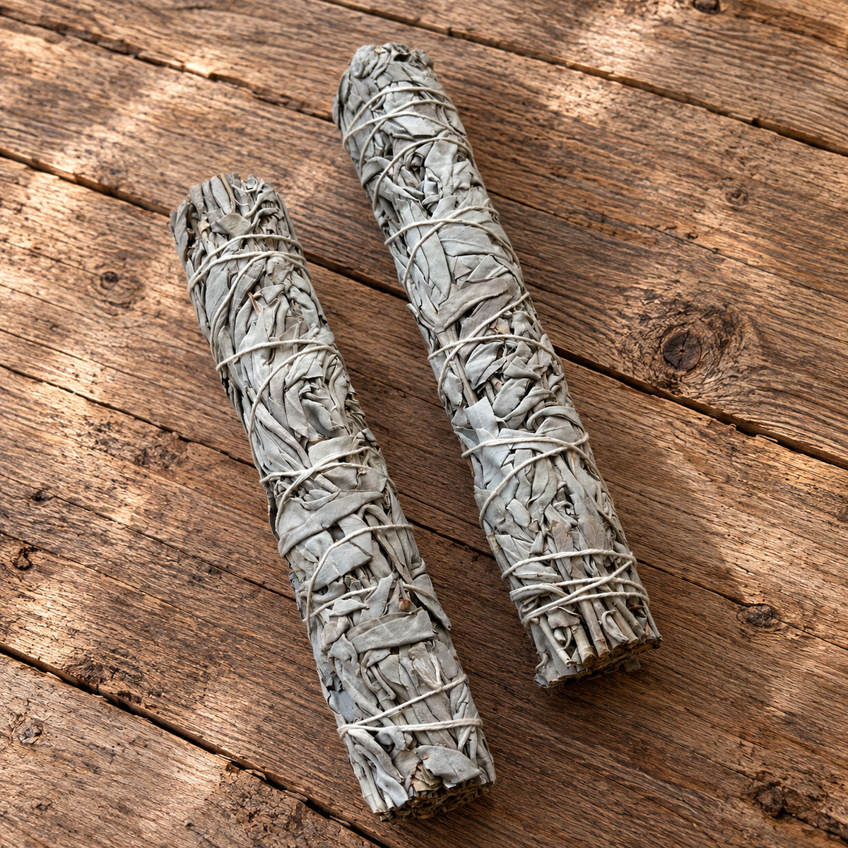 Two long, dried natural white sage smudge bundles tied with natural cord on wood