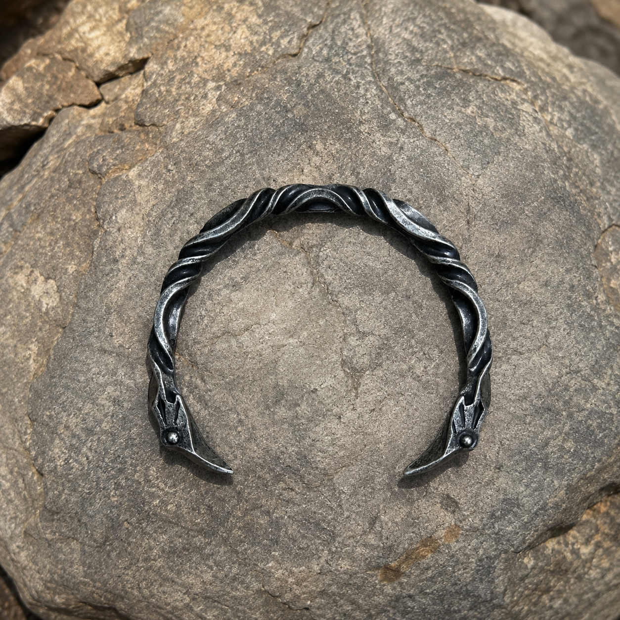 Nordic raven head open cuff bracelet with twisted forged design displayed on rock.