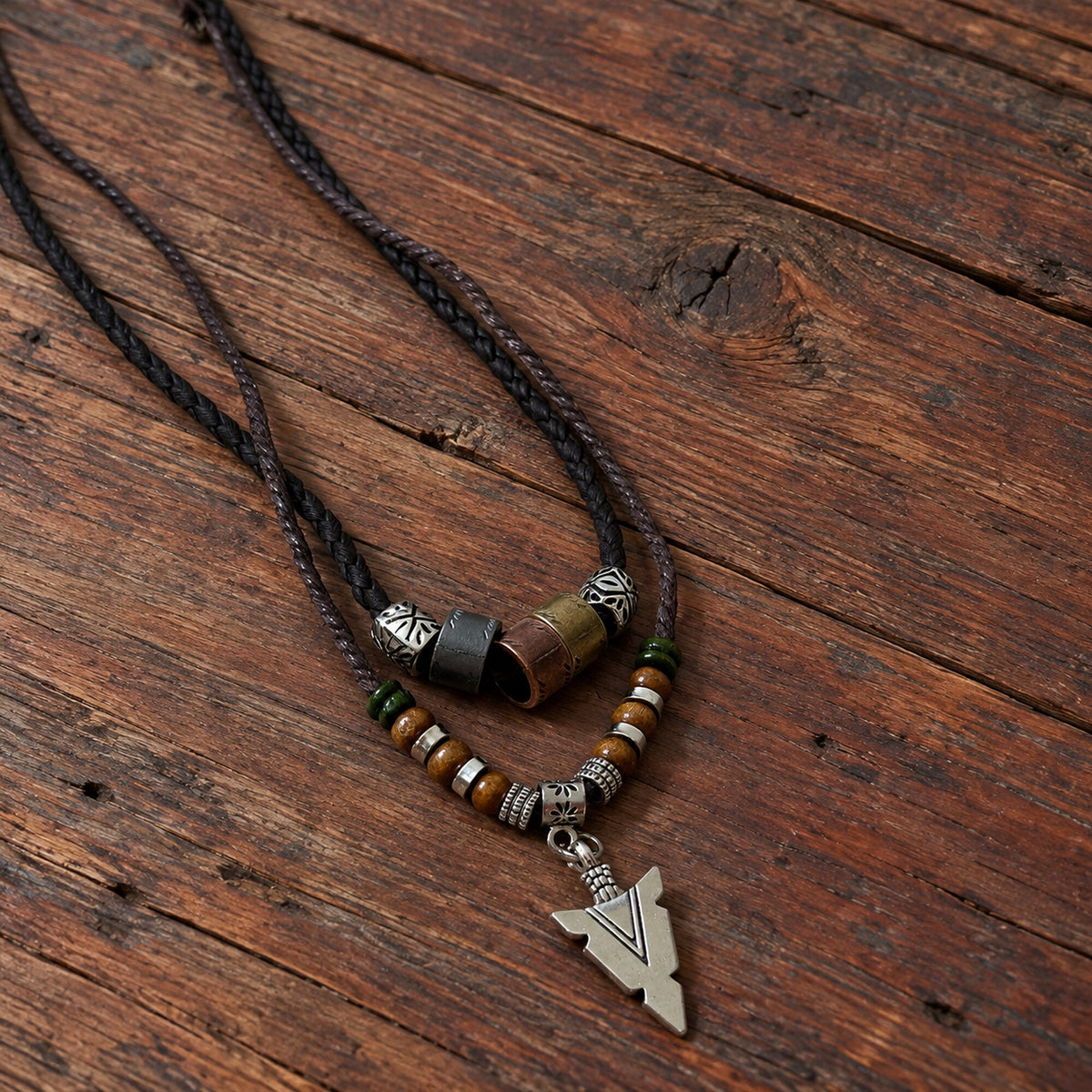 Brown cord Norse-inspired arrow amulet necklace with layered beadwork displayed on rustic wooden surface.