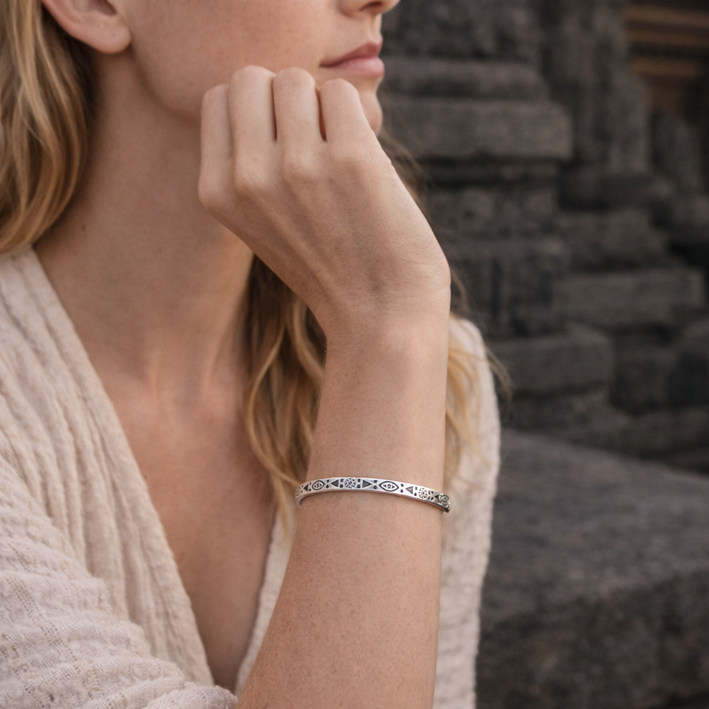 Model wearing the Padang Padang Pulse Cuff Bracelet, a slim silver-tone open cuff with repeating eye motifs