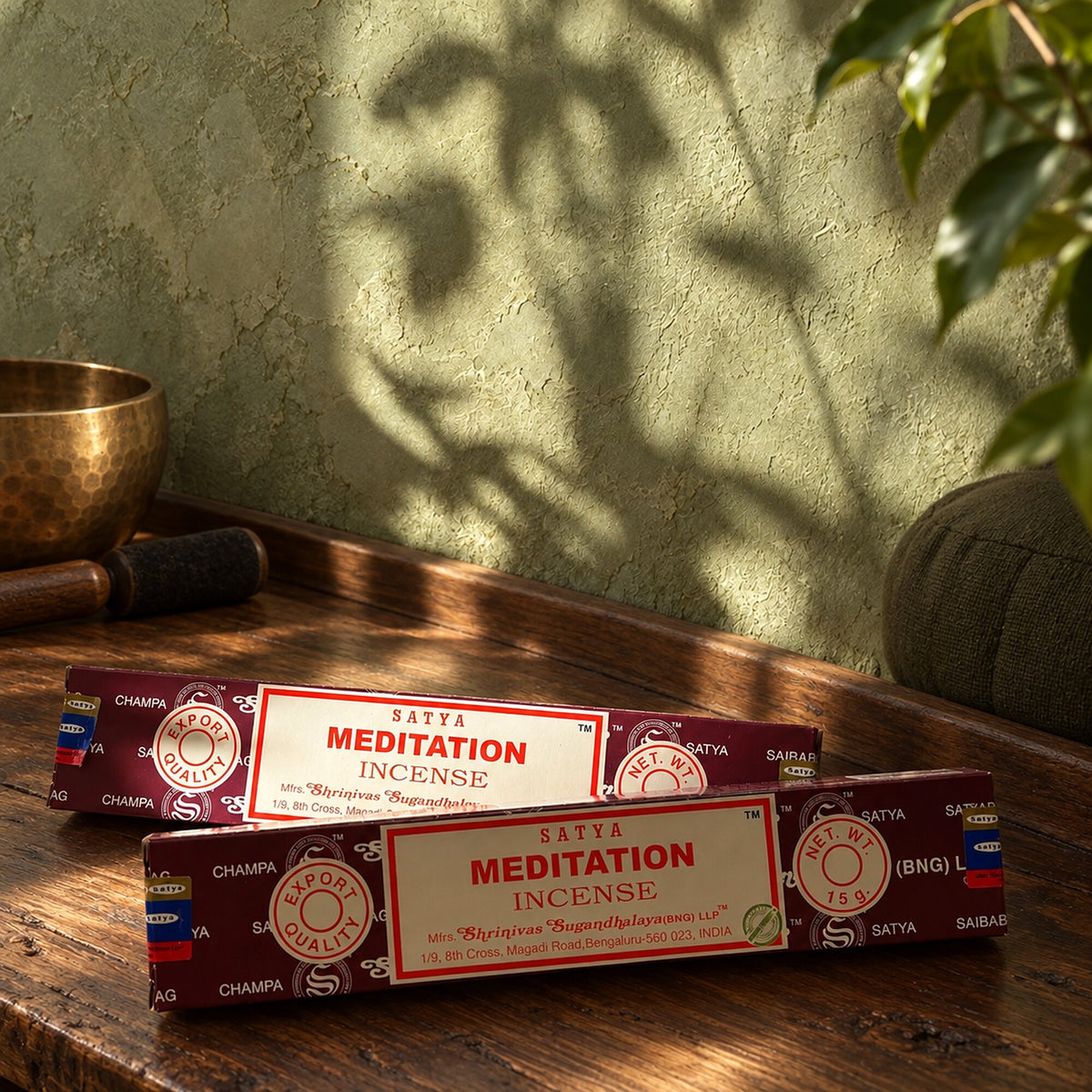 Two Satya Meditation incense stick boxes in burgundy packaging, 15g, displayed on a wooden table in a sunlit meditation-inspired setting.
