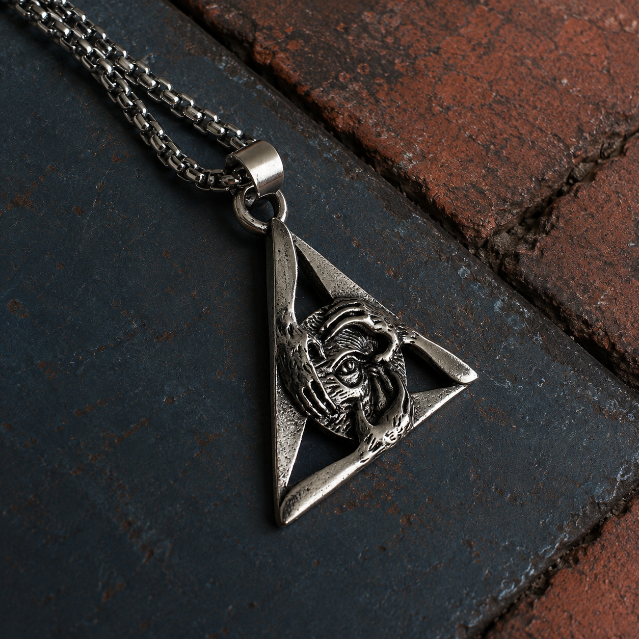 Close-up of silver-tone triangular pendant featuring an eye framed by sculpted hands.