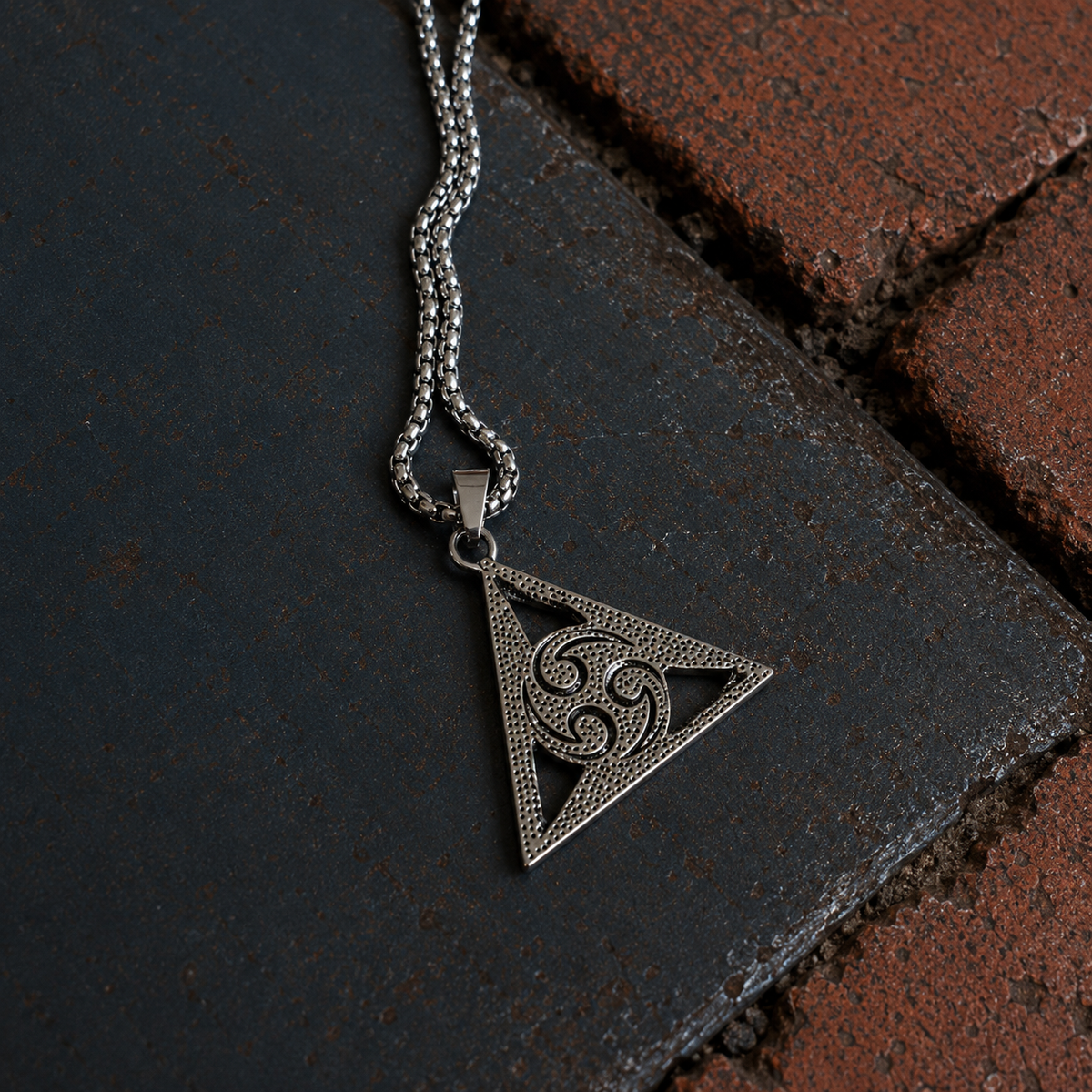 Reverse of silver-tone all seeing eye triangle pendant featuring an ornamental triple-spiral design